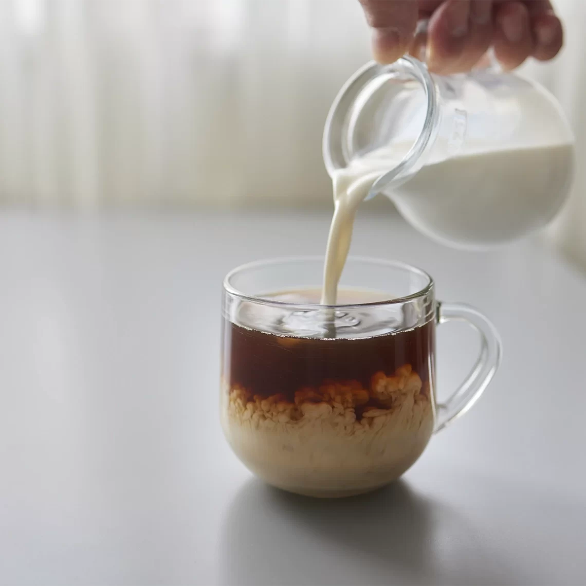 Foto mostrando as mãos de um barista acrescentando leite em um café gelado