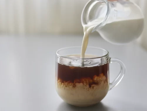 Foto mostrando as mãos de um barista acrescentando leite em um café gelado